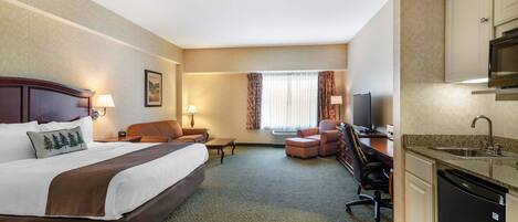 A hotel room with a large bed, a desk, a chair, a television, a microwave, and a sink.