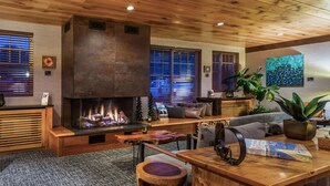 A cozy living room with a fireplace, wooden furniture, and a large window with blinds. - Maine Evergreen Hotel, an Ascend Collection Hotel (Augusta)
