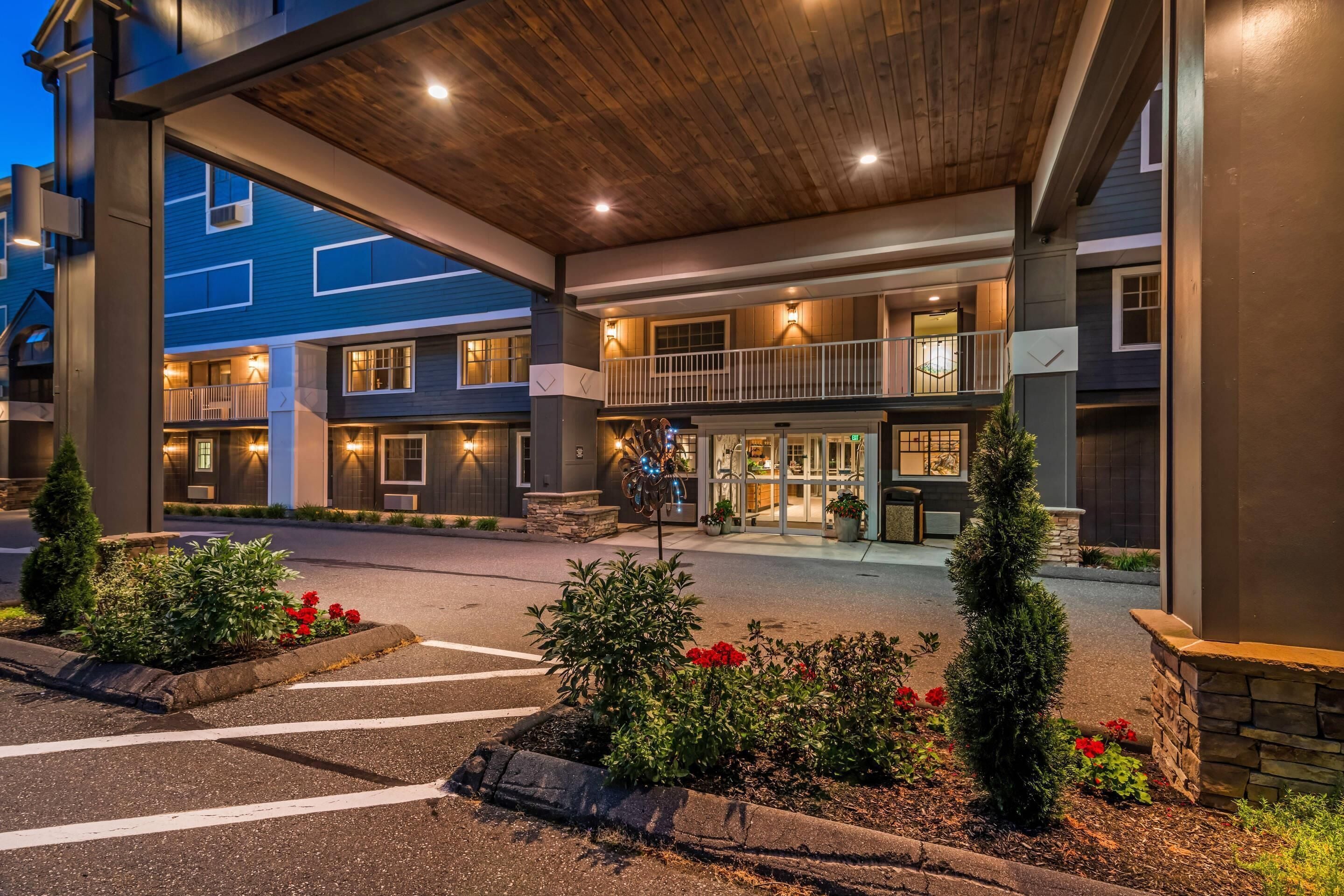 A multi-story hotel with a covered entrance, outdoor seating, and a landscaped area with plants and flowers.