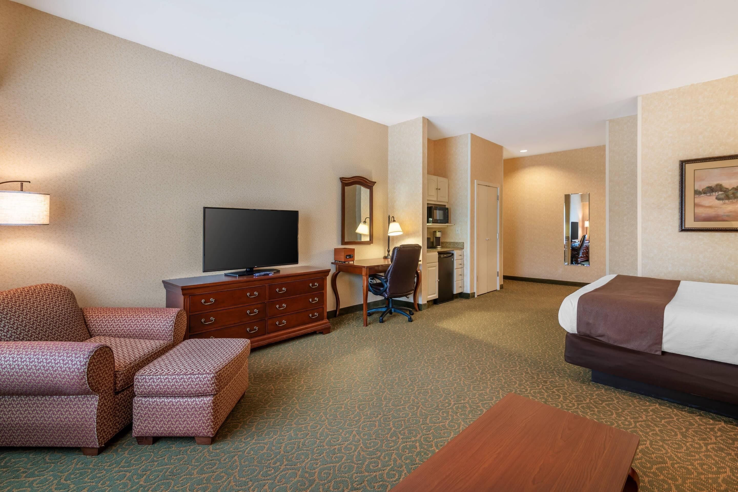A hotel room with a bed, a desk with a computer, a television, a chair, a dresser, and a lamp.