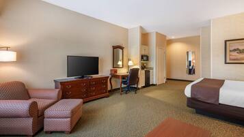 A hotel room with a bed, a desk with a computer, a television, a chair, a dresser, and a lamp.