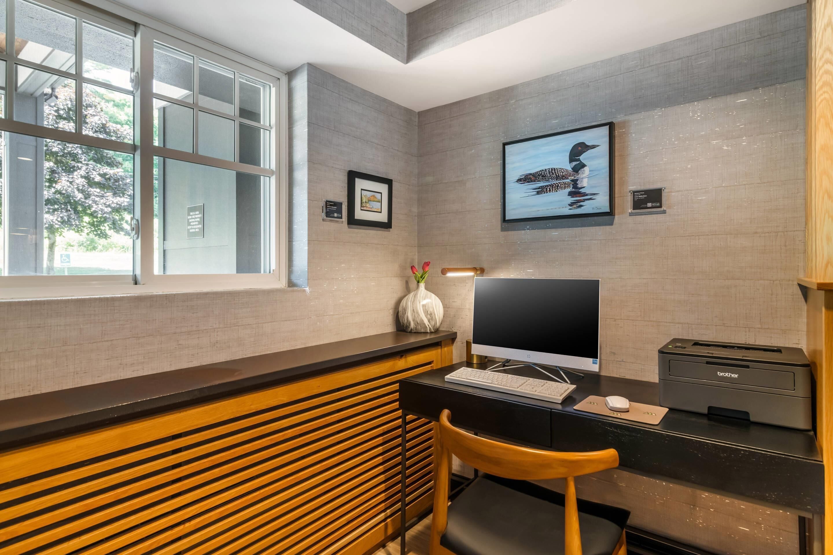 Een moderne kantoorruimte met een bureau, computer, printer en een raam met zonwering.