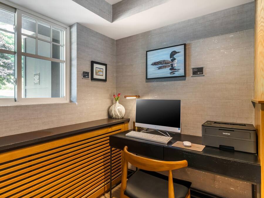 A modern office space with a desk, computer, printer, and a window with blinds.