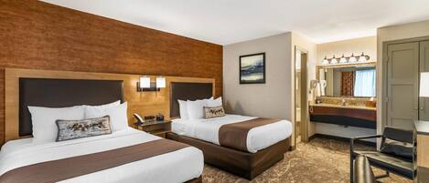 A hotel room with two beds, a large mirror, a vanity with a sink, and a chair.