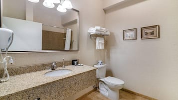 A bathroom with a granite countertop sink, a mirror, a toilet, and two framed pictures on the wall.