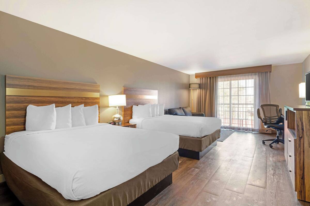 A hotel room with two beds, a desk, a chair, and a large window.