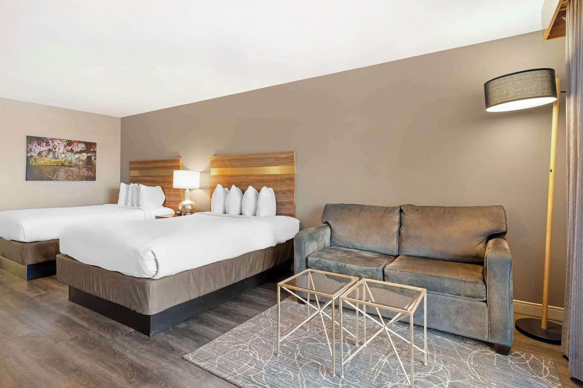 A hotel room with two beds, a sofa, a lamp, and a decorative headboard.