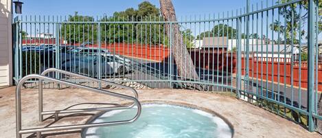A hot tub with metal railings and a metal fence, surrounded by a parking area and a tree.
