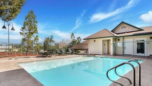 A swimming pool with a metal ladder, surrounded by a fence, trees, and a building with a tiled roof. - Best Western Cedar Inn & Suites (Angels Camp)