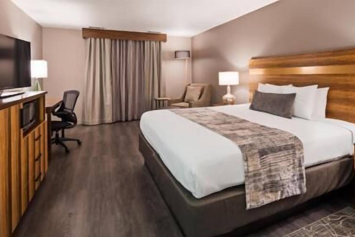 A hotel room with a bed, a desk, a chair, a TV, and a window with curtains.