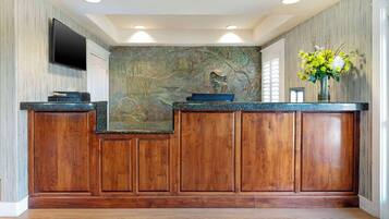 Un área de recepción con un mostrador de madera, un televisor de pantalla plana montado en la pared y un mural decorativo.