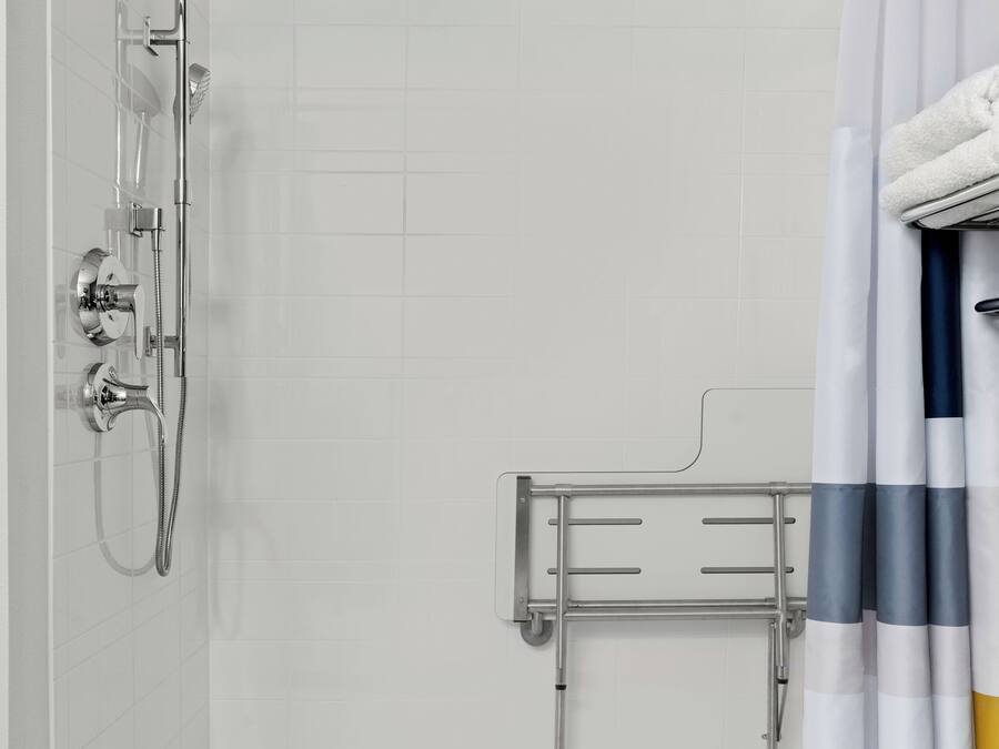 Ducha con cabezal de ducha manual, zona de ducha con mampara de vidrio y asiento para la ducha.
