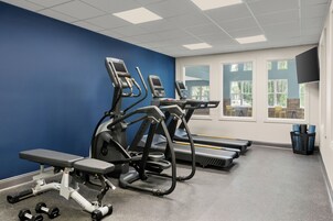 Un gimnasio con cintas de correr, un banco y pesas.