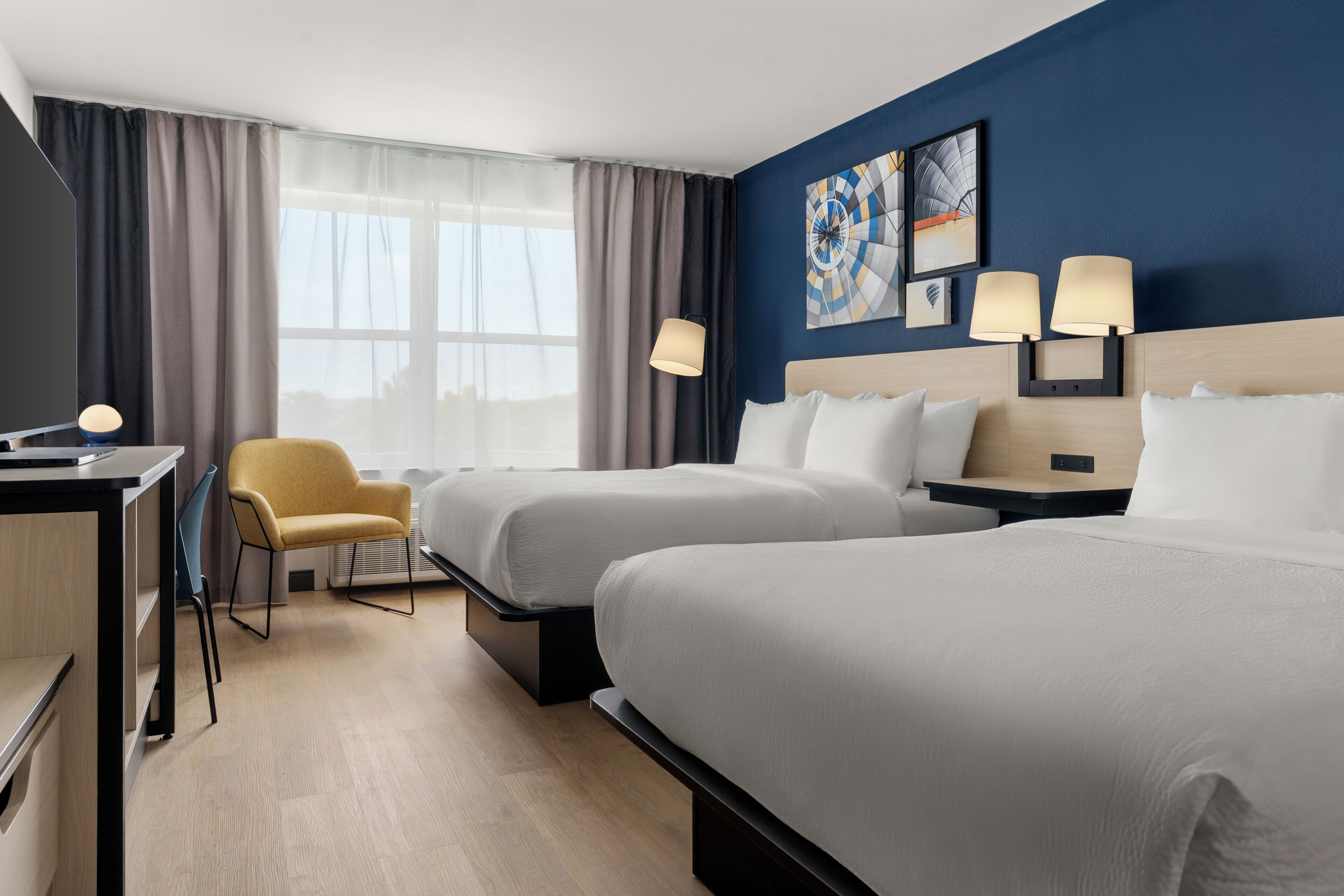 A hotel room with two beds, a desk, a chair, and a window with curtains.