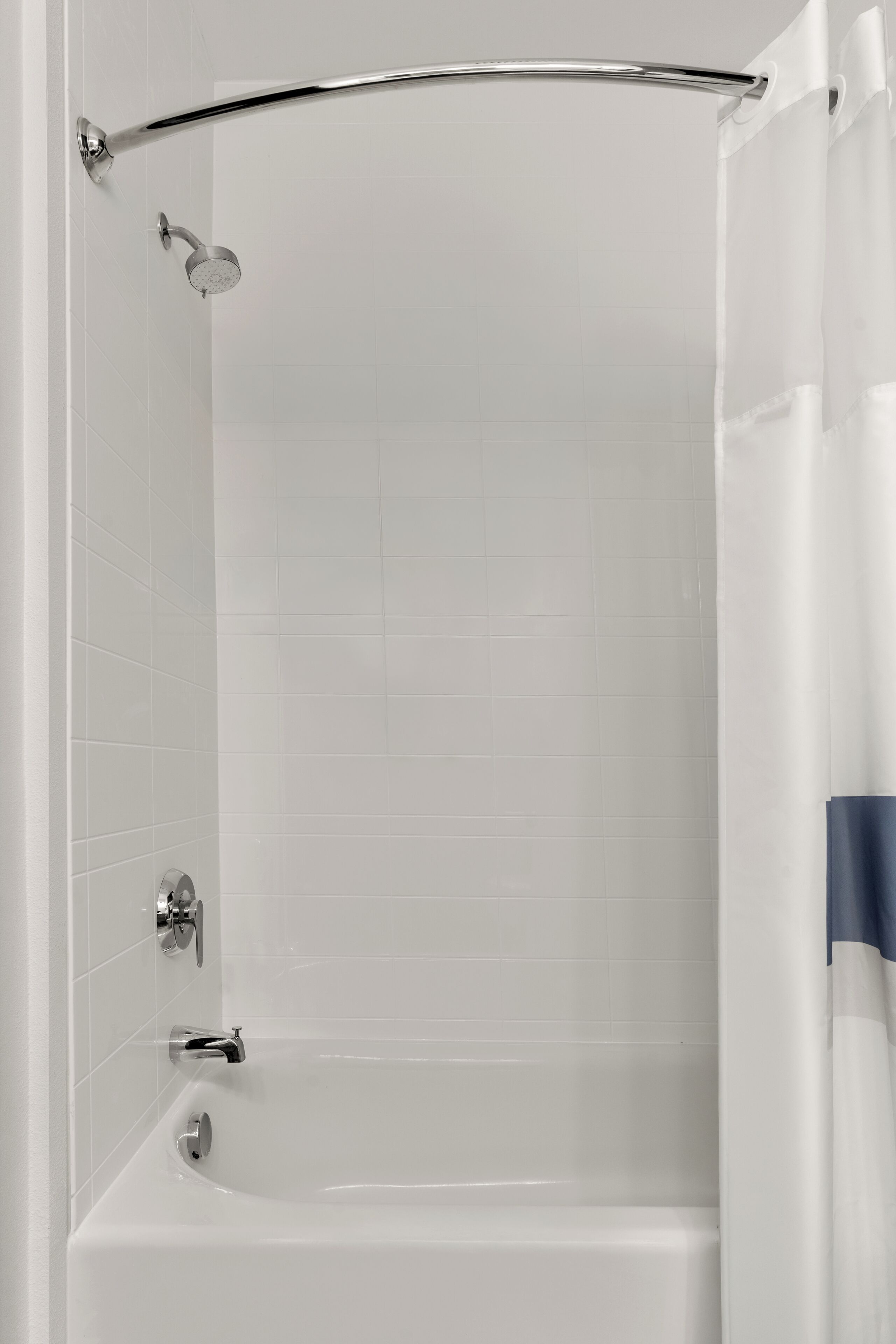 Una bañera blanca con ducha, grifo y cortina, con paredes de azulejos.