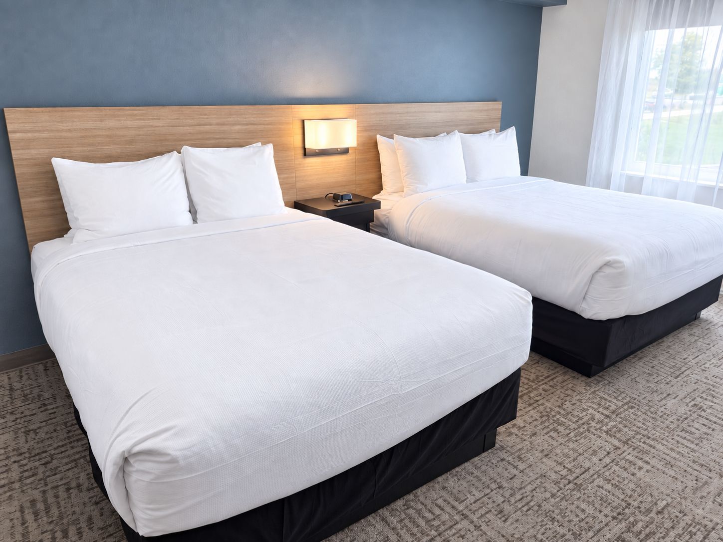 Two adjacent beds with white linens, a wooden headboard, a nightstand with a lamp, and a carpeted floor.