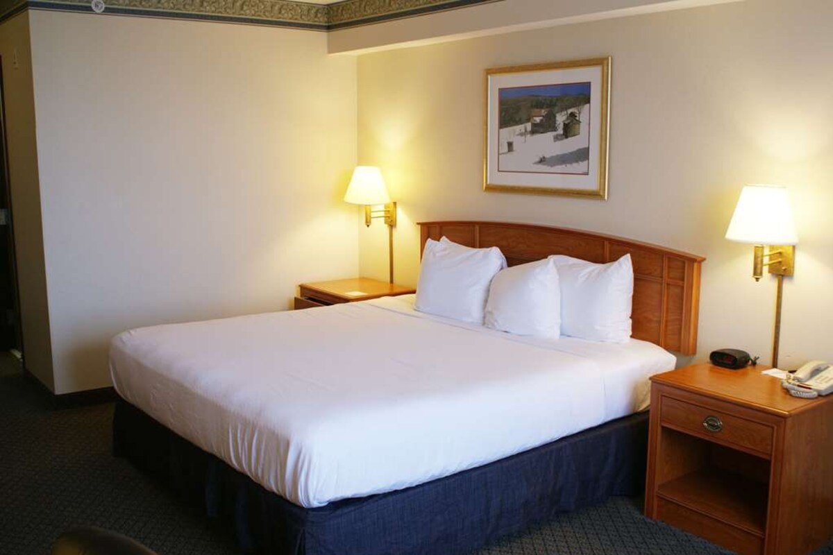 A hotel room with a large bed, two bedside tables, a nightstand, and a framed picture on the wall.