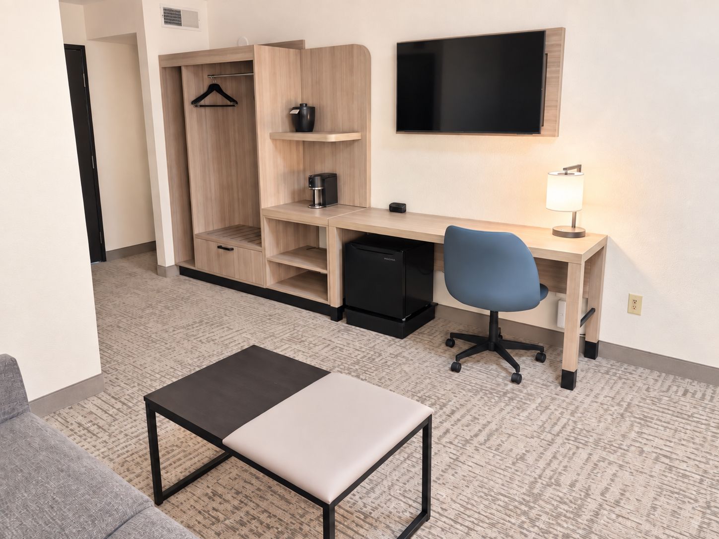 A hotel room with a desk, chair, and a television mounted on the wall.