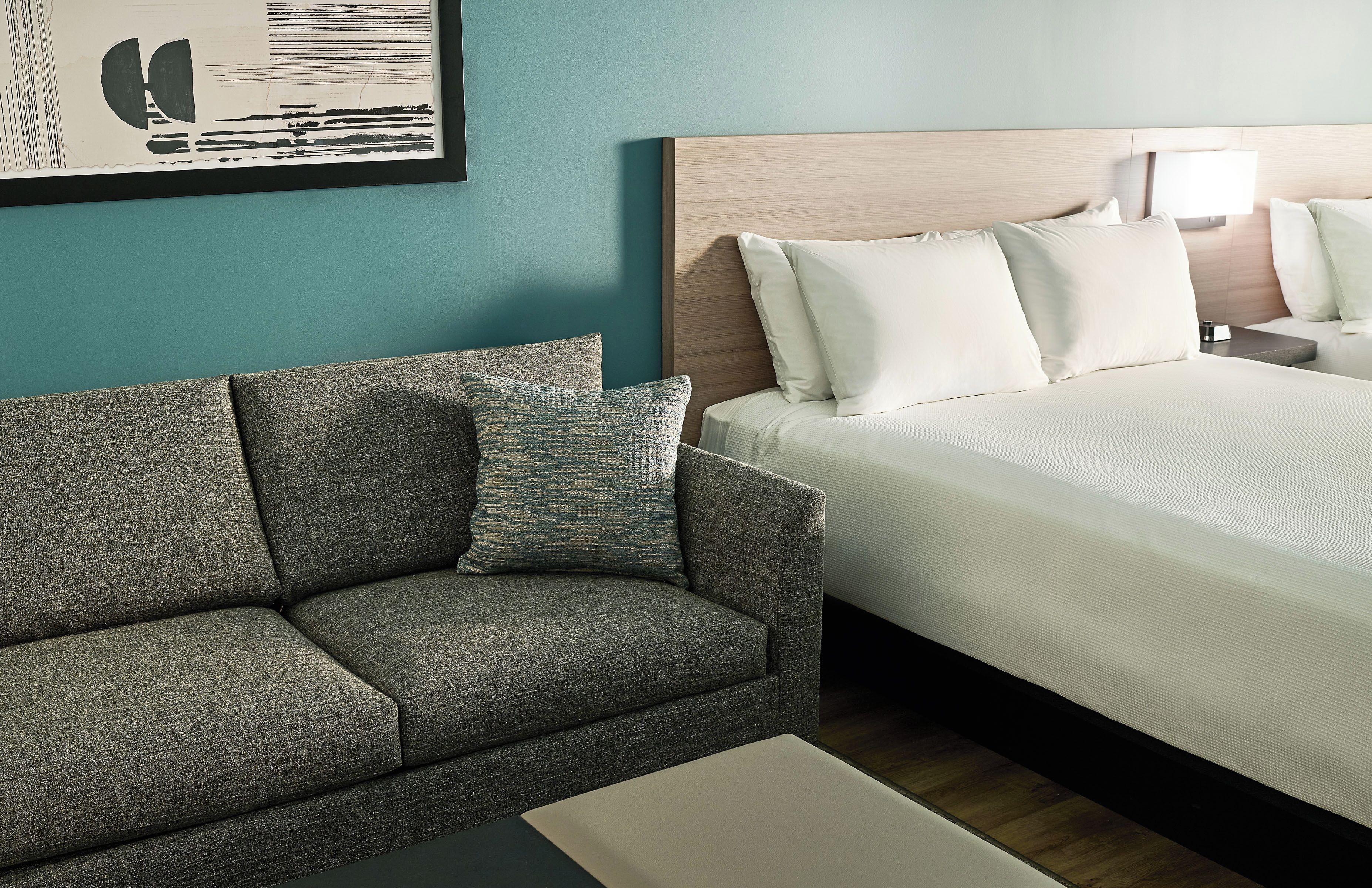 A hotel room with a bed, a sofa, a nightstand, a lamp, and a framed picture on the wall.