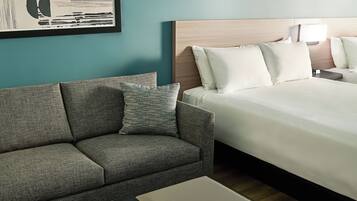 A hotel room with a bed, a sofa, a nightstand, a lamp, and a framed picture on the wall.