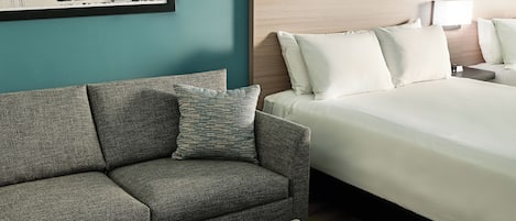 Una habitación de hotel con una cama, un sofá, una mesita de noche, una lámpara y un cuadro en la pared.