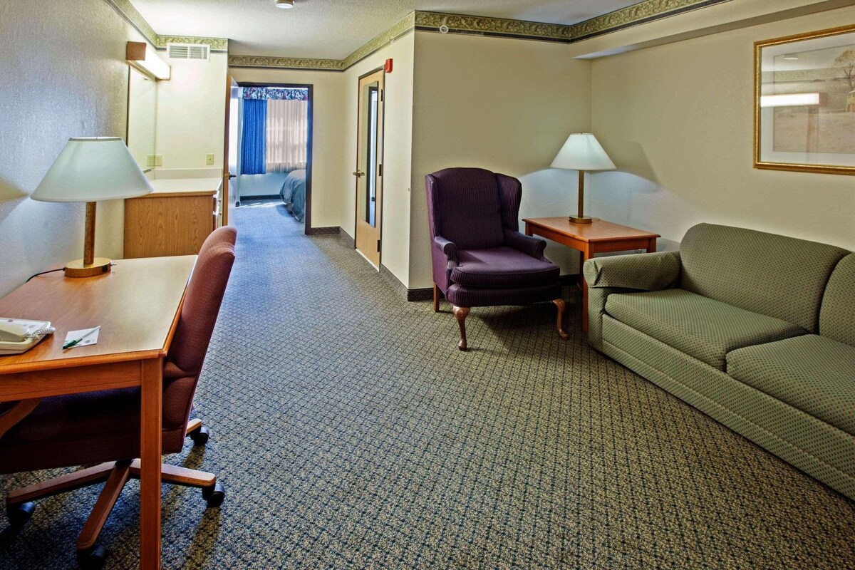 A hotel room with a wooden desk, a purple armchair, a green sofa, and two bedside lamps.