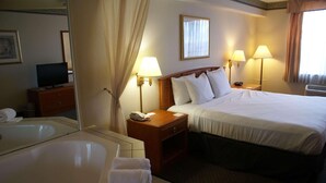 A hotel room with a large bed, two bedside lamps, a nightstand with a phone, a mirror, a television, and a bathtub with towels.