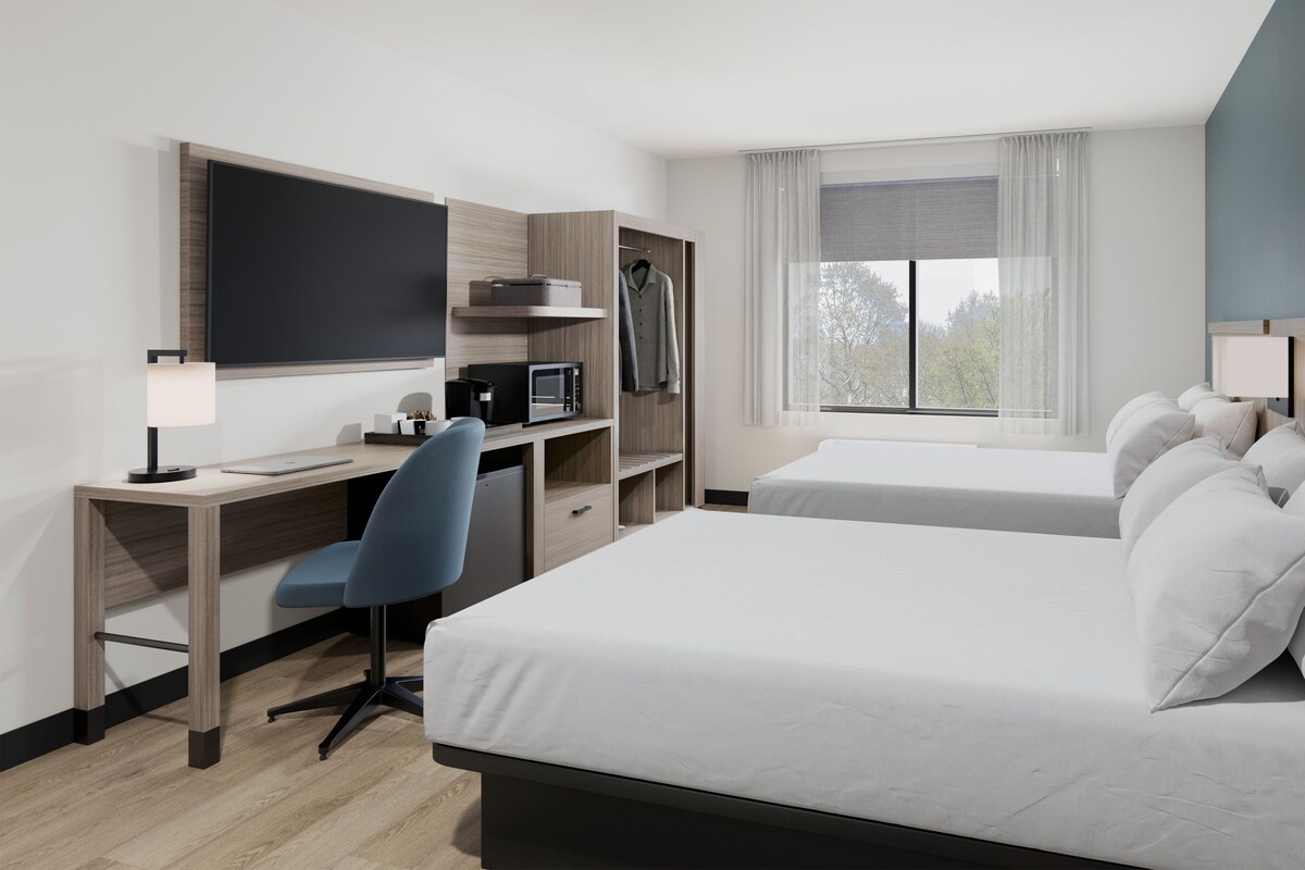 A hotel room with a bed, desk, chair, and a TV.