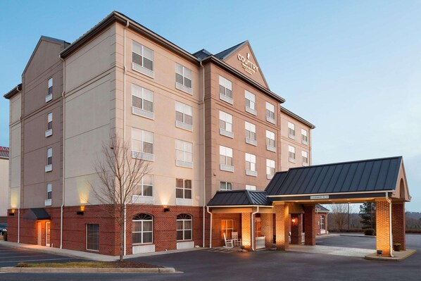 A multi-story hotel with a brick facade, a covered entrance, and a parking lot.