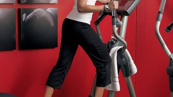 A woman using a stationary bike in a gym with red walls and multiple exercise machines.