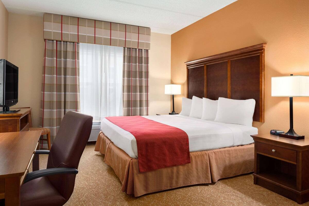 A hotel room with a large bed, two bedside lamps, a wooden nightstand, a desk with a chair, and a television.