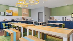 A modern café with wooden tables and benches, a kitchen area, and a green wall with artwork. - Spark by Hilton Indianapolis Northeast Fishers (Fishers)