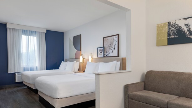 A hotel room with two beds, a sofa, and artwork on the walls. - Spark by Hilton Indianapolis Northeast Fishers (Fishers)