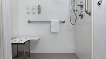 Un baño con azulejos blancos, un perchero, una ducha con cabezal de ducha manual y una mesita pequeña.