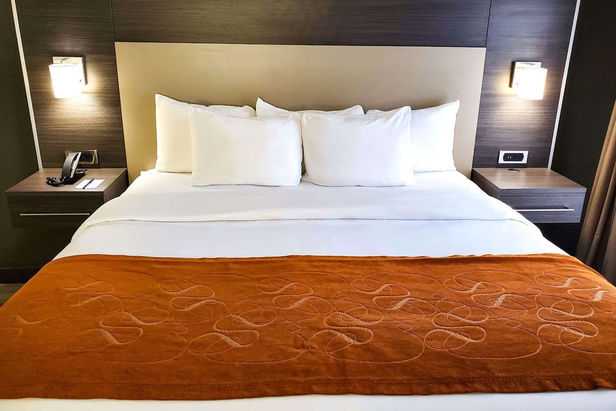 A hotel room with a bed, white pillows, a brown blanket, and two bedside lamps.