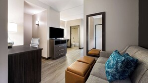 Ein modernes Hotelzimmer mit Flachbildfernseher, Schreibtisch, einer Couch mit Kissen und einem großen Spiegel.