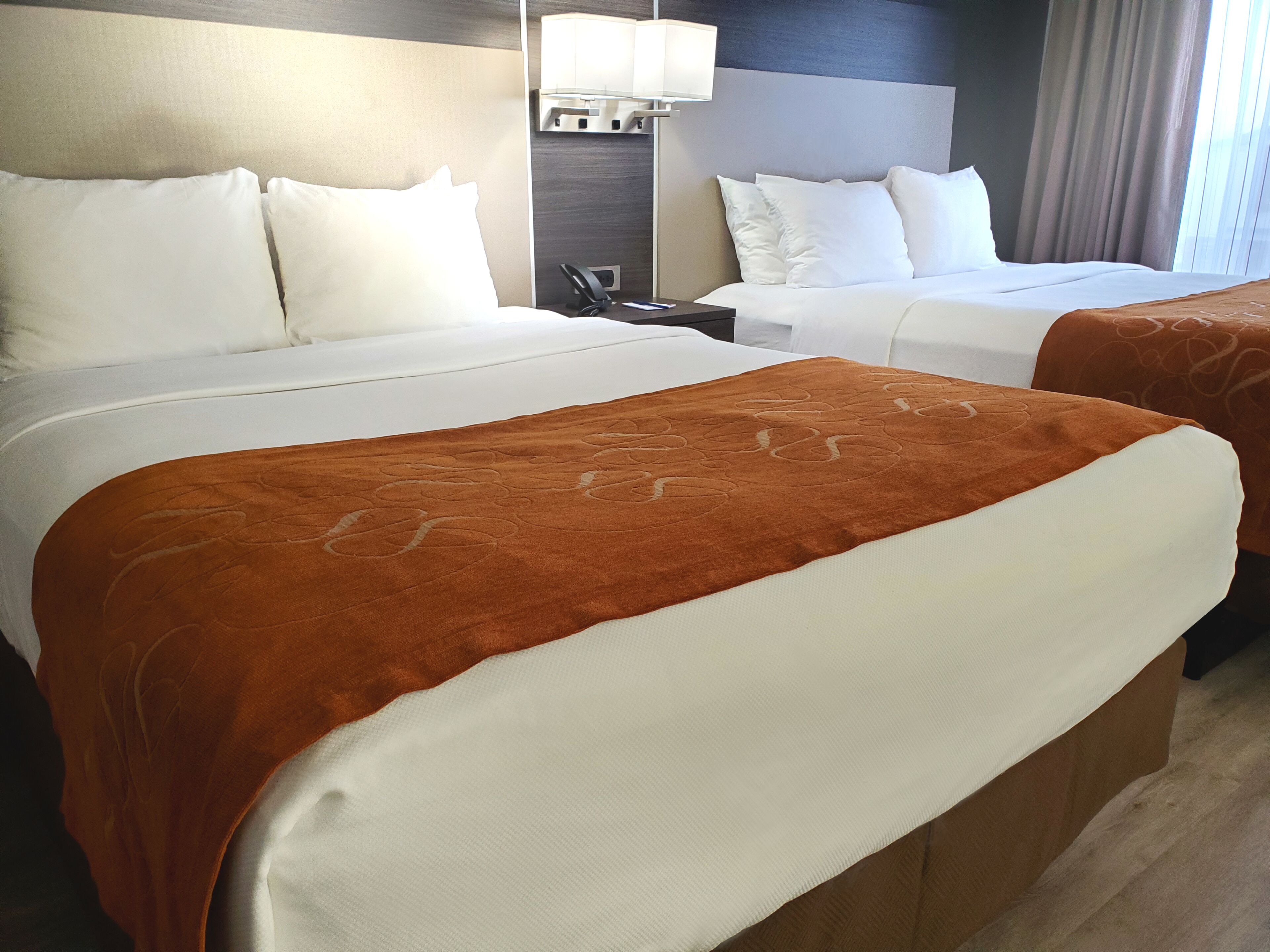 A hotel room with two beds, a nightstand, a lamp, and a window with curtains.