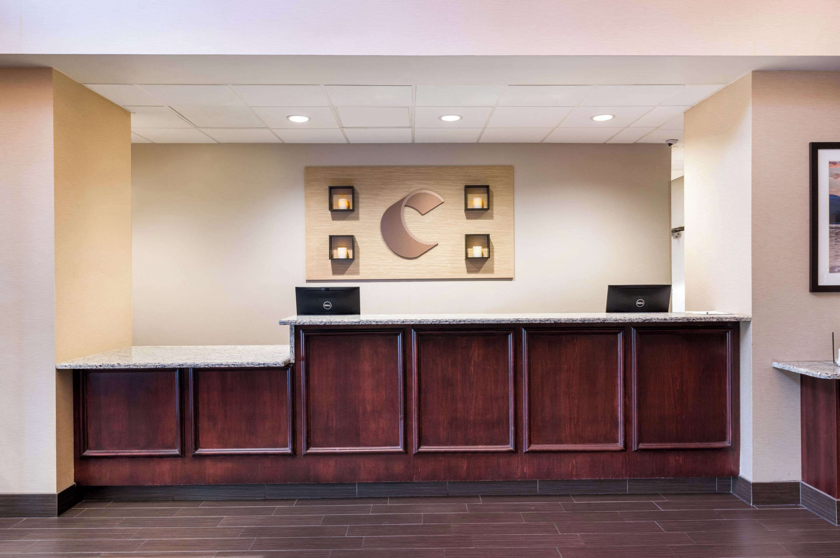 A reception desk with a wooden panel design, a large illuminated letter 'C', and two laptops on the counter.