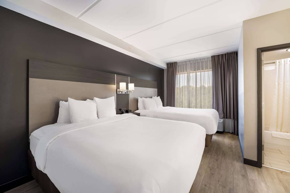 A hotel room with two beds, a large mirror, and a view of the outdoors.