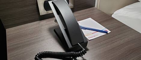 A hotel room with a bedside telephone, a notepad, and a pen on the nightstand.