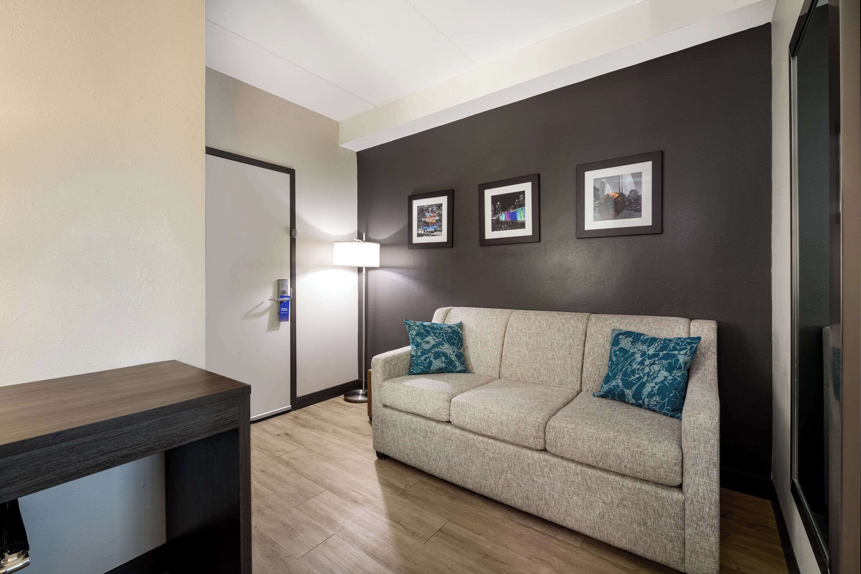 Un salon moderne avec un canapé beige, deux coussins à motifs, une lampe sur pied et trois tableaux encadrés accrochés au mur.