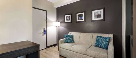 Un salon moderne avec un canapé beige, deux coussins à motifs, une lampe sur pied et trois tableaux encadrés accrochés au mur.