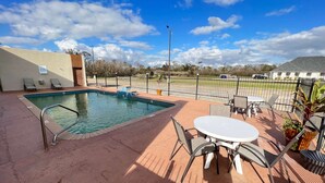 An outdoor pool area with a table and chairs, surrounded by a fence, and a building in the background. - Days Inn by Wyndham Rayne/Crowley (Rayne)