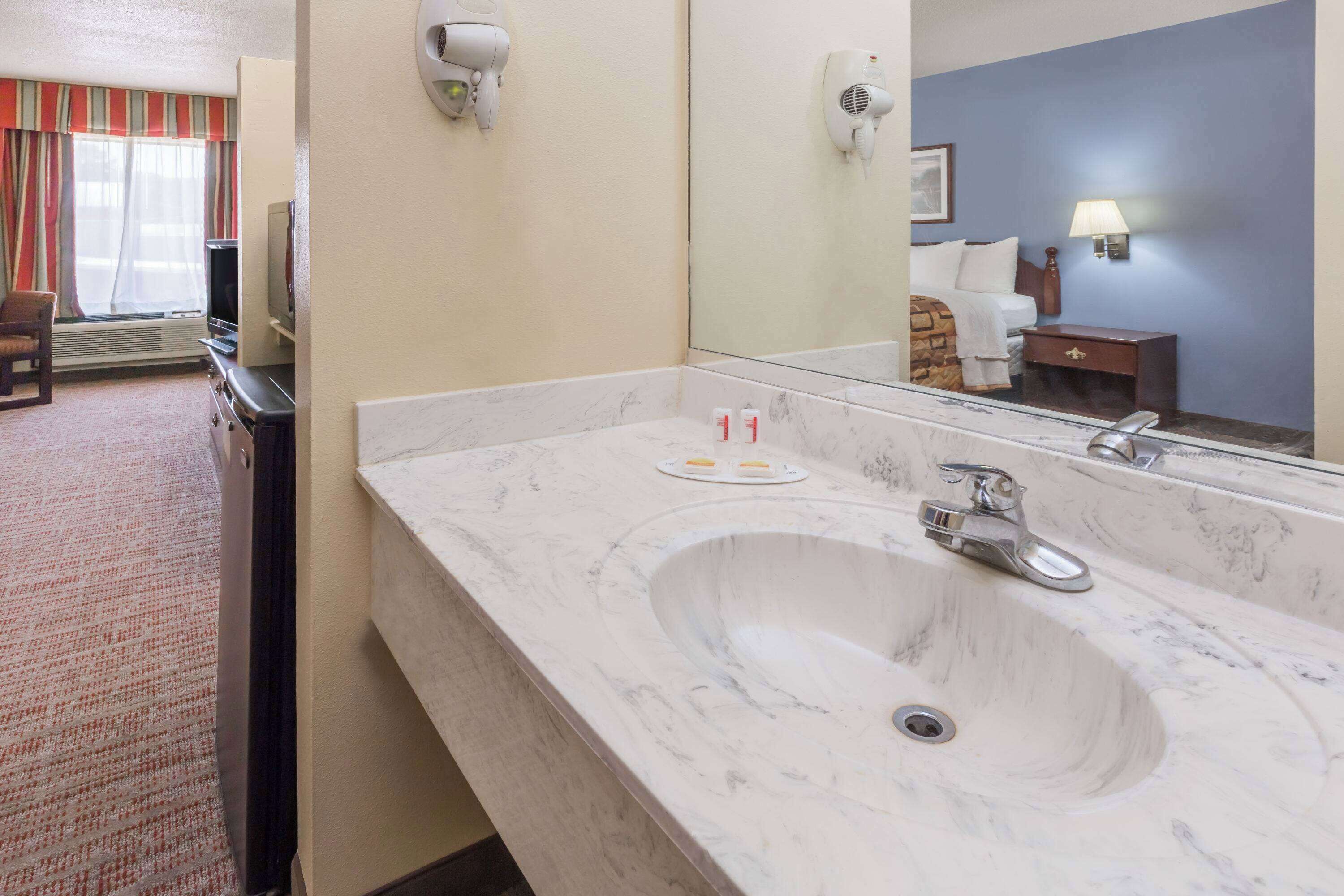 A hotel bathroom with a large marble sink, a mirror, a hairdryer, and a television in the corner.