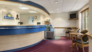A reception area with a blue counter, a clock, and a television on the wall. There are wooden chairs and a small table with a water dispenser. - Days Inn by Wyndham Michaelwood M5 (Berkeley)