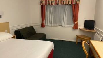 A hotel room with a bed, a sofa, a desk with a computer, and a window with curtains.