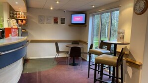 A restaurant interior with a counter, chairs, a television displaying 'heart', and a clock on the wall. - Days Inn by Wyndham Michaelwood M5 (Berkeley)