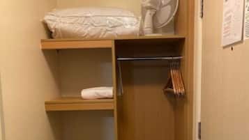 Habitación pequeña con literas, un ventilador, perchero y una puerta con un aviso.