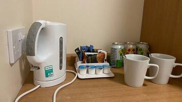 A kitchenette with a coffee maker, a mug rack, and a can of soda.