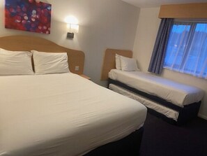 A hotel room with a large bed, a smaller bed, a nightstand, a lamp, a painting on the wall, and a window with curtains. - Days Inn by Wyndham Michaelwood M5 (Berkeley)